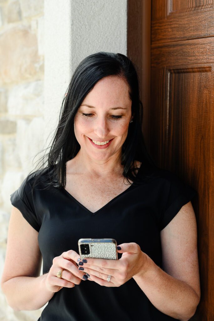A woman small business owner smiles down at her phone as captured by a Denver Branding photographer for her branding photos.