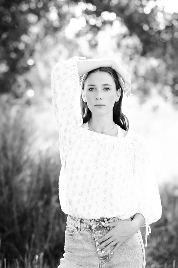 A black and white senior picture of a girl standing with a white shirt with puffy sleeves looking with a model face at a Denver senior photographer.
