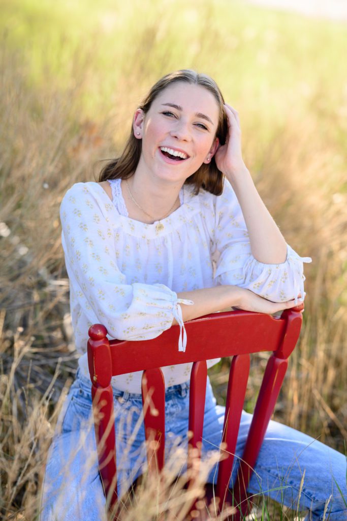 Denver Senior Photographer captures a young brunette sitting backwards in a red chair.