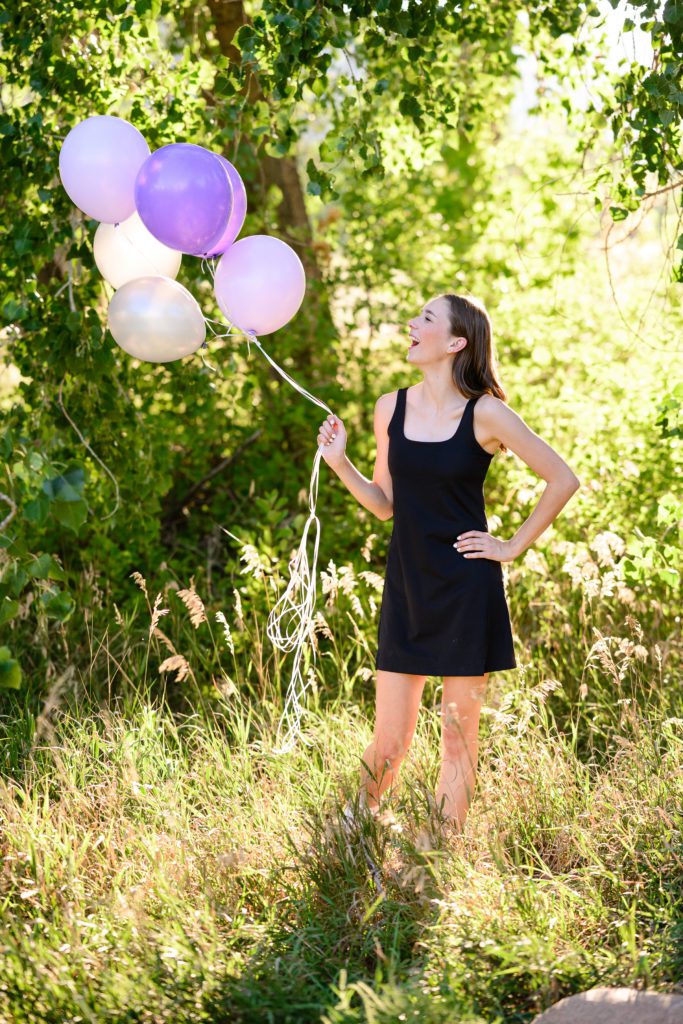 A girl in a black dress holding a bunch of purple balloons for a Denver Senior Photographer