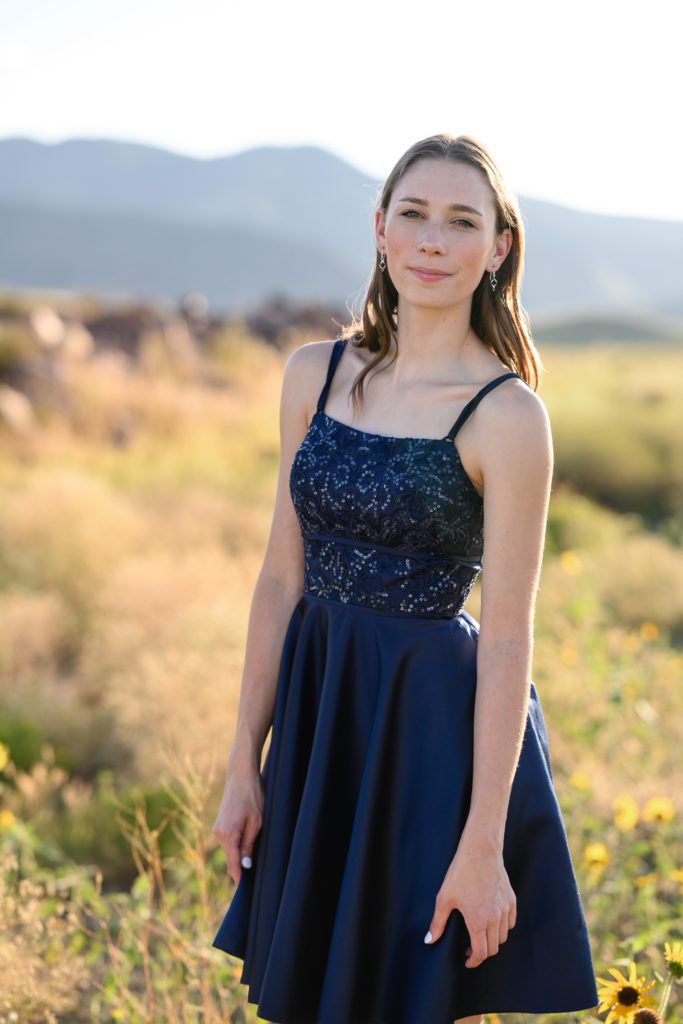 A Denver Senior photographer captures a girl in a fancy blue dress smirking at the camera in iconic colorado scenery.