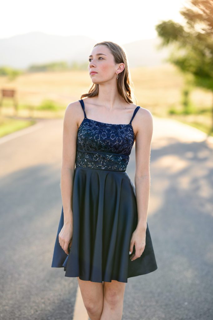 A girl in a fancy blue dress with sparkles and spaghetti straps looking away from a Denver senior photographer with a mountain scene in the background.