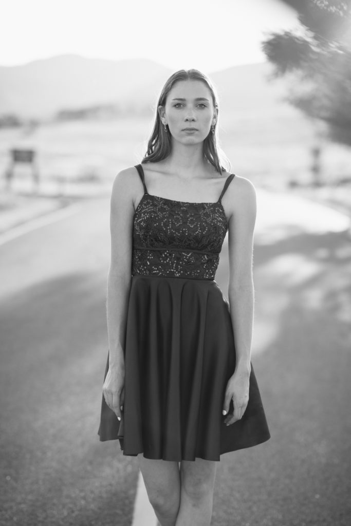A black and white image of a senior girl in a fancy dress standing in the middle of the road for her senior pictures.