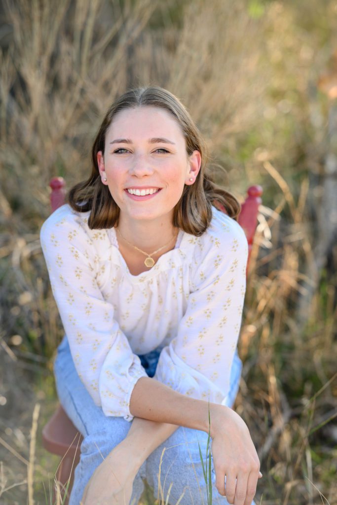 Denver Senior Photographer captures a senior girl sitting on a chair leaning forward and smiling.