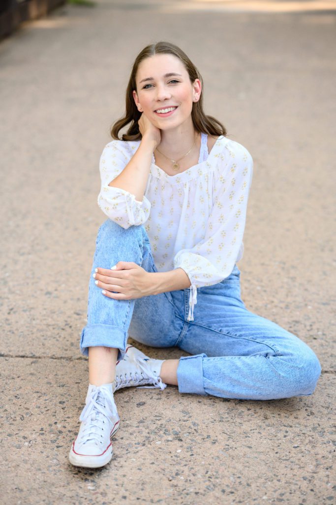 Denver Senior Photographer captures a senior girl in a cute outfit sitting on the ground with one knee up.