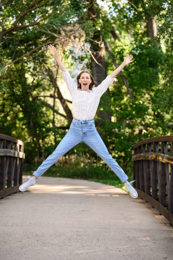 Young senior girl jumping up with arms and legs fully extended toward a Denver senior photographer