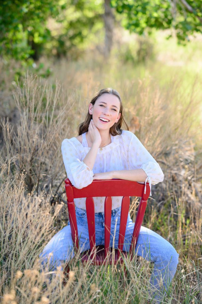 Denver senior photos for a girl with dark hair in jeans and a white peasant top sitting in a red chair.