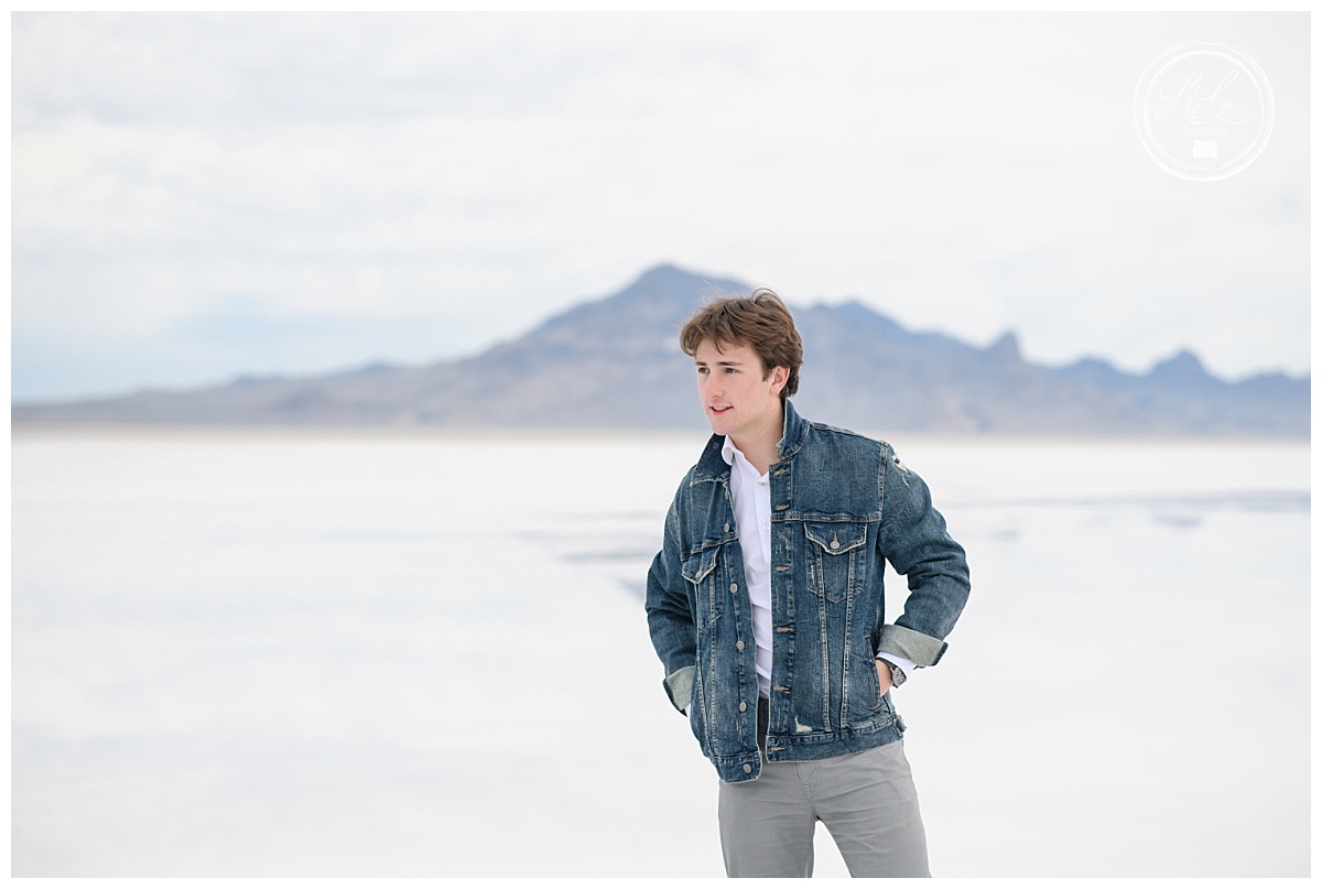 Denver Photography Locations with boy standing in salt flats with mountains behind him while wearing a jean jacket with his hands in his pockets