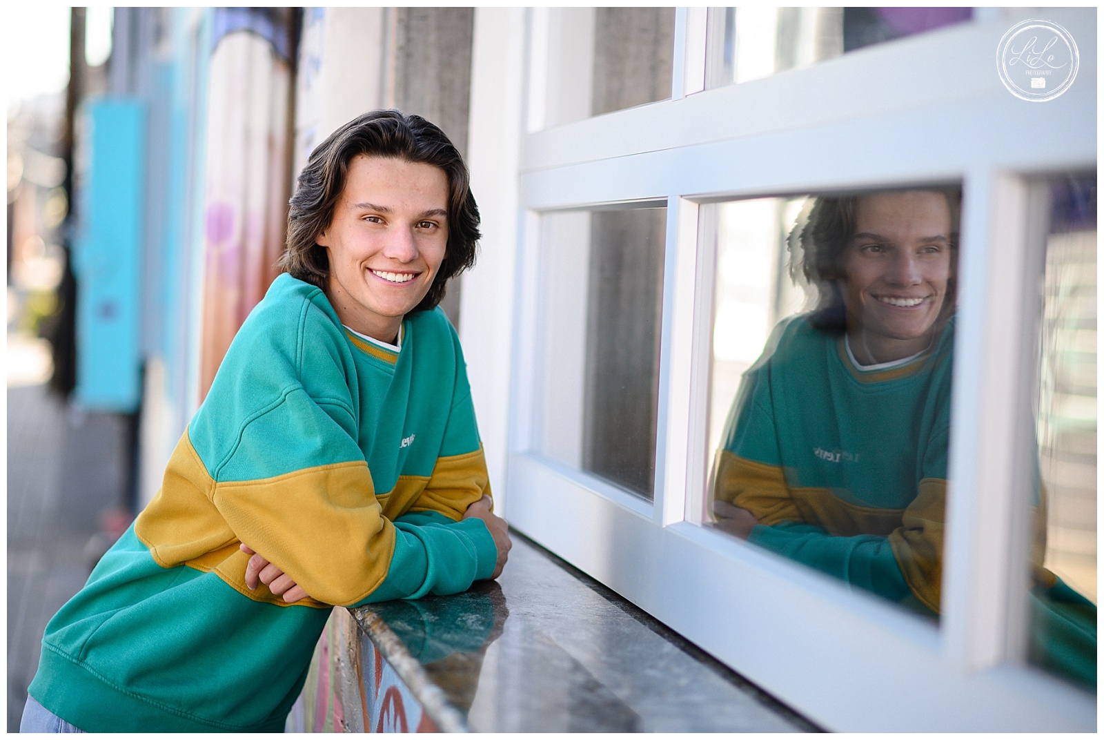 denver commercial photographers capture senior student against garage door wearing green and yellow sweatshirt in downtown denvers rino district