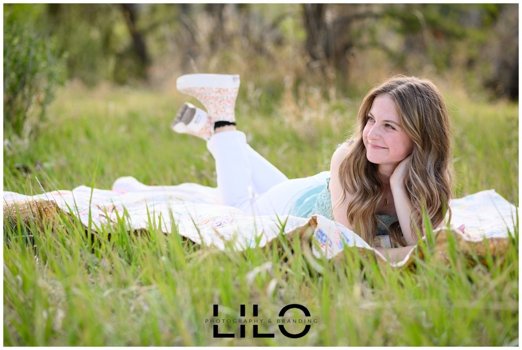A senior girl laying on a blanket looking off to the side and smiling away from a Denver senior photographer for her Denver senior photos.