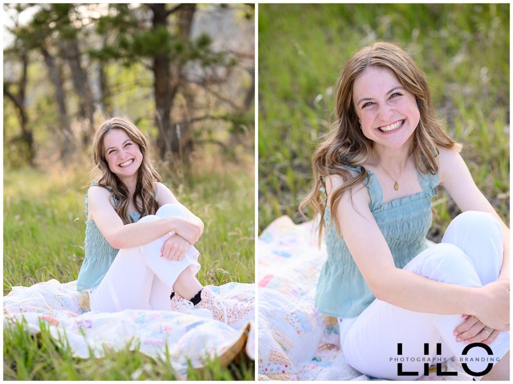 Denver Senior Photos for a girl with blonde hair sitting on a quilt in the middle of a meadow of greenery at Lair O the Bear park captured by a Denver Senior Photographer.