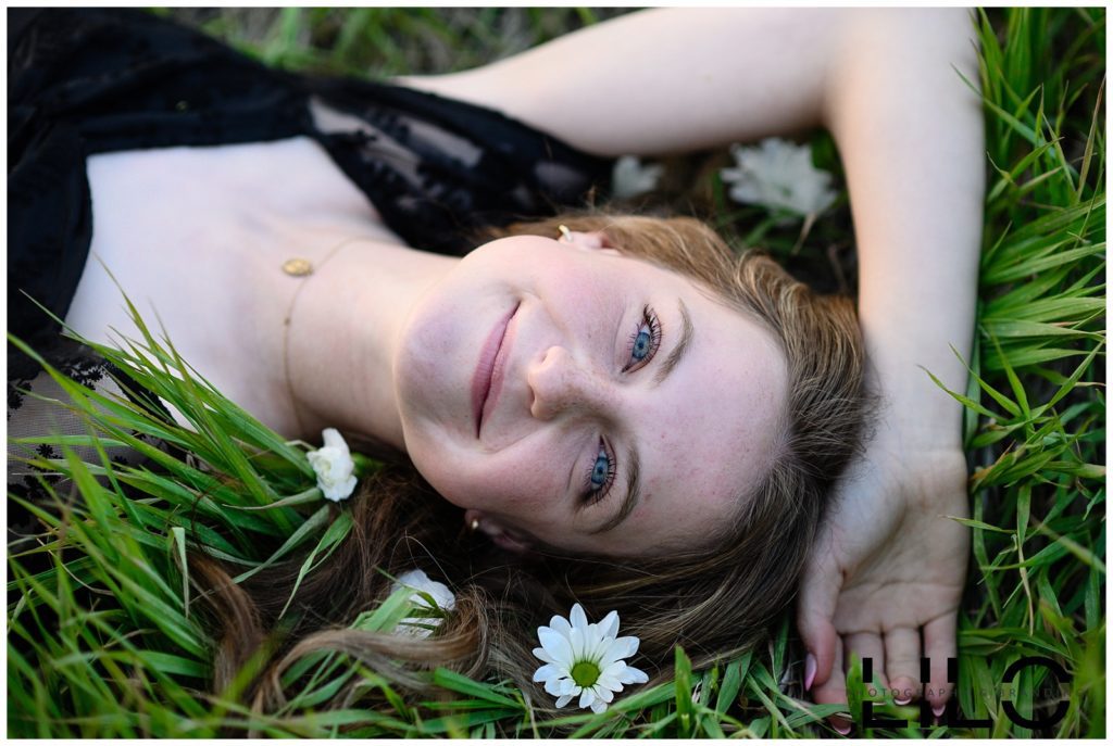 A girl laying in the grass with flowers all around her smiling up at a denver senior photographer.