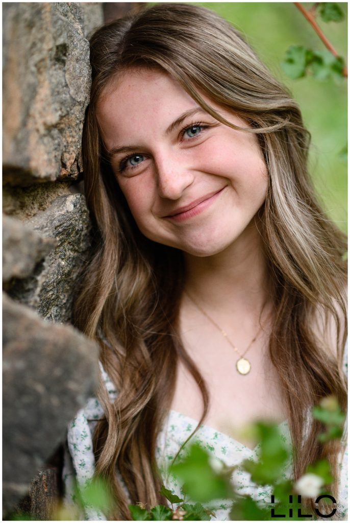 Littleton Senior Pictures for a girl leaning against a rock wall with greenery all around.