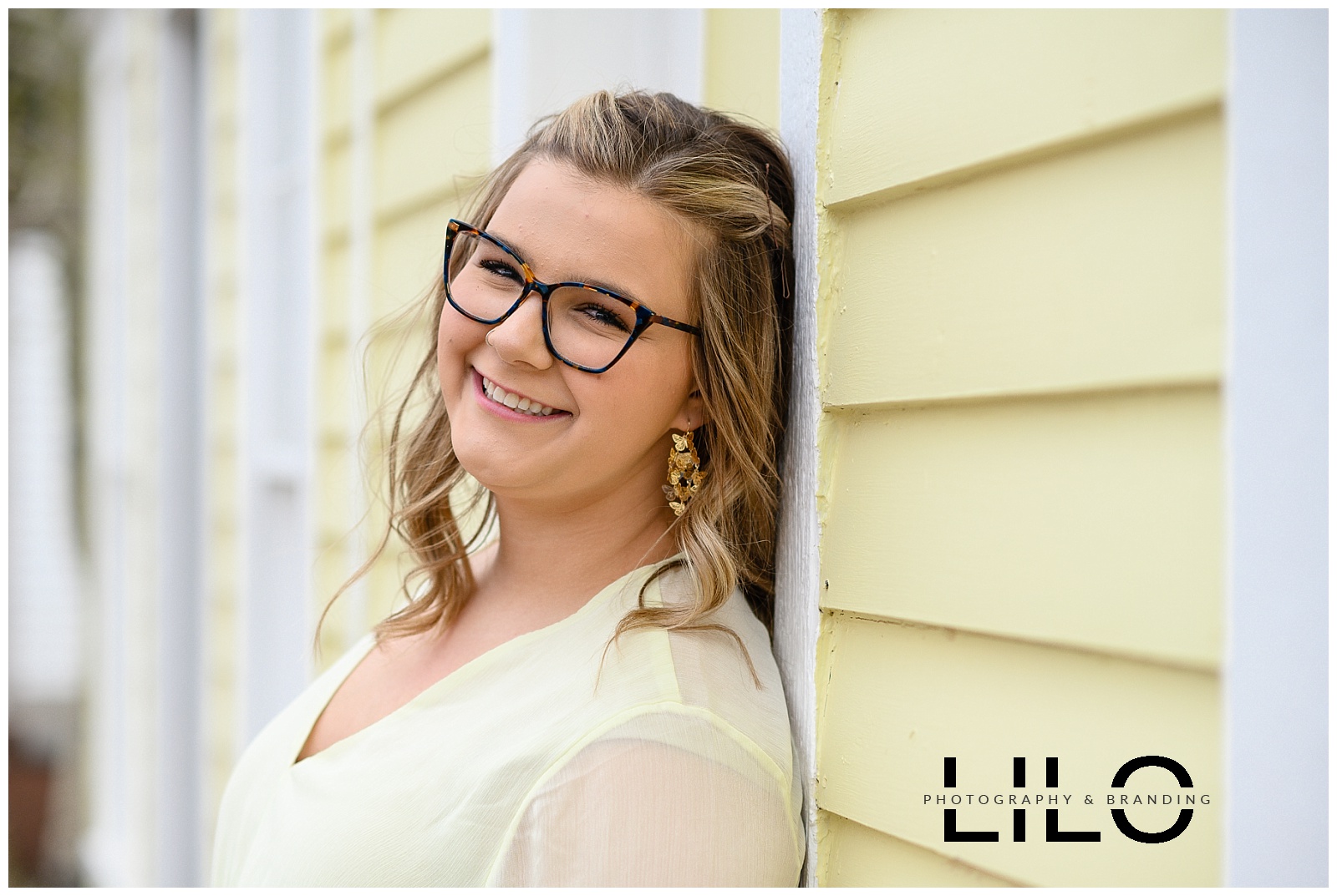 Senior photo of girl wearing glasses, wearing yellow against a yellow wall captured by denver commercial photographers