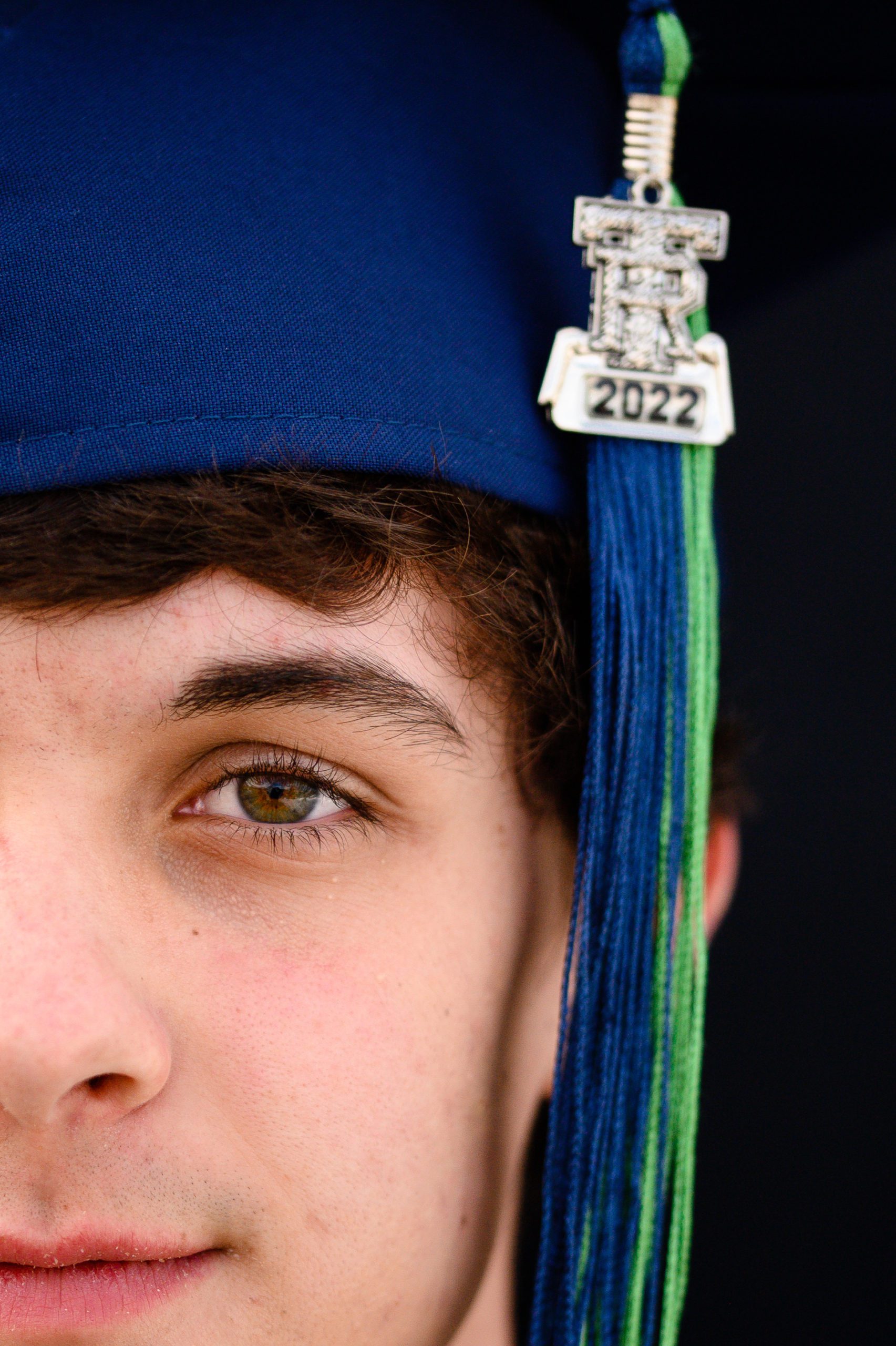 Denver Senior Photographer closeup of a senior boy half face with brown eyes and a blue graduation cap and tassle that says TR 2022.
