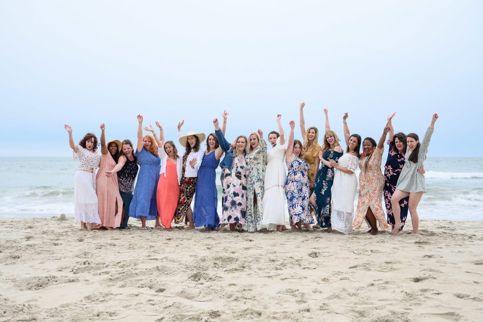 A long line of women on a beach in bright clothing with their arms raised in celebration for Denver Commercial Photographers.