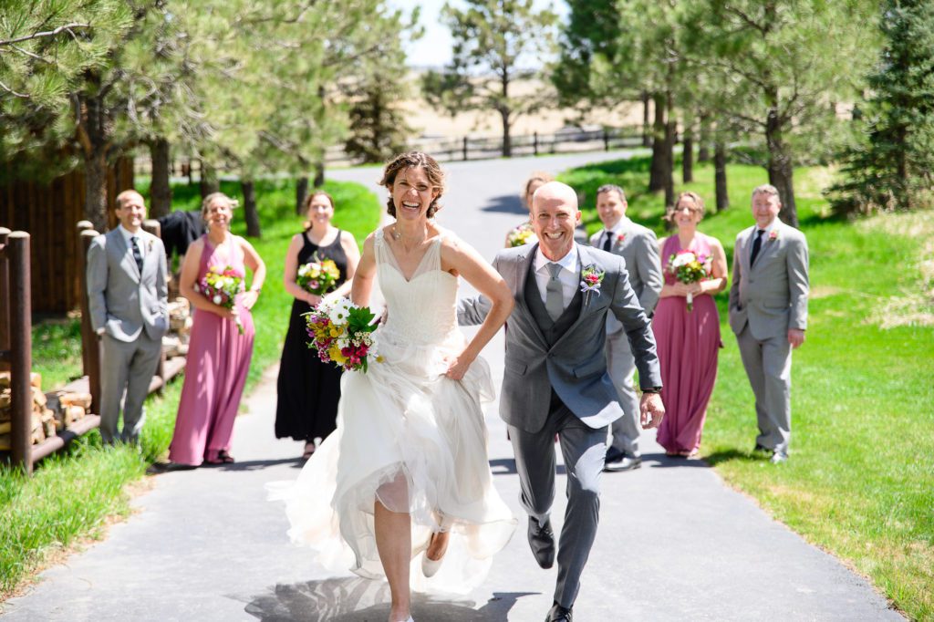 Bride and groom running at a Denver Photographer while the wedding party smiles in the background.