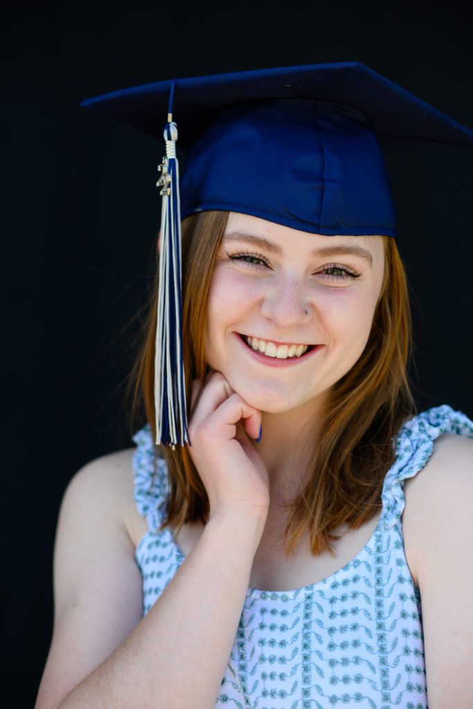 A girl in a blue graduation cap with her hand on her chin smiling at a Denver Senior Photographer.