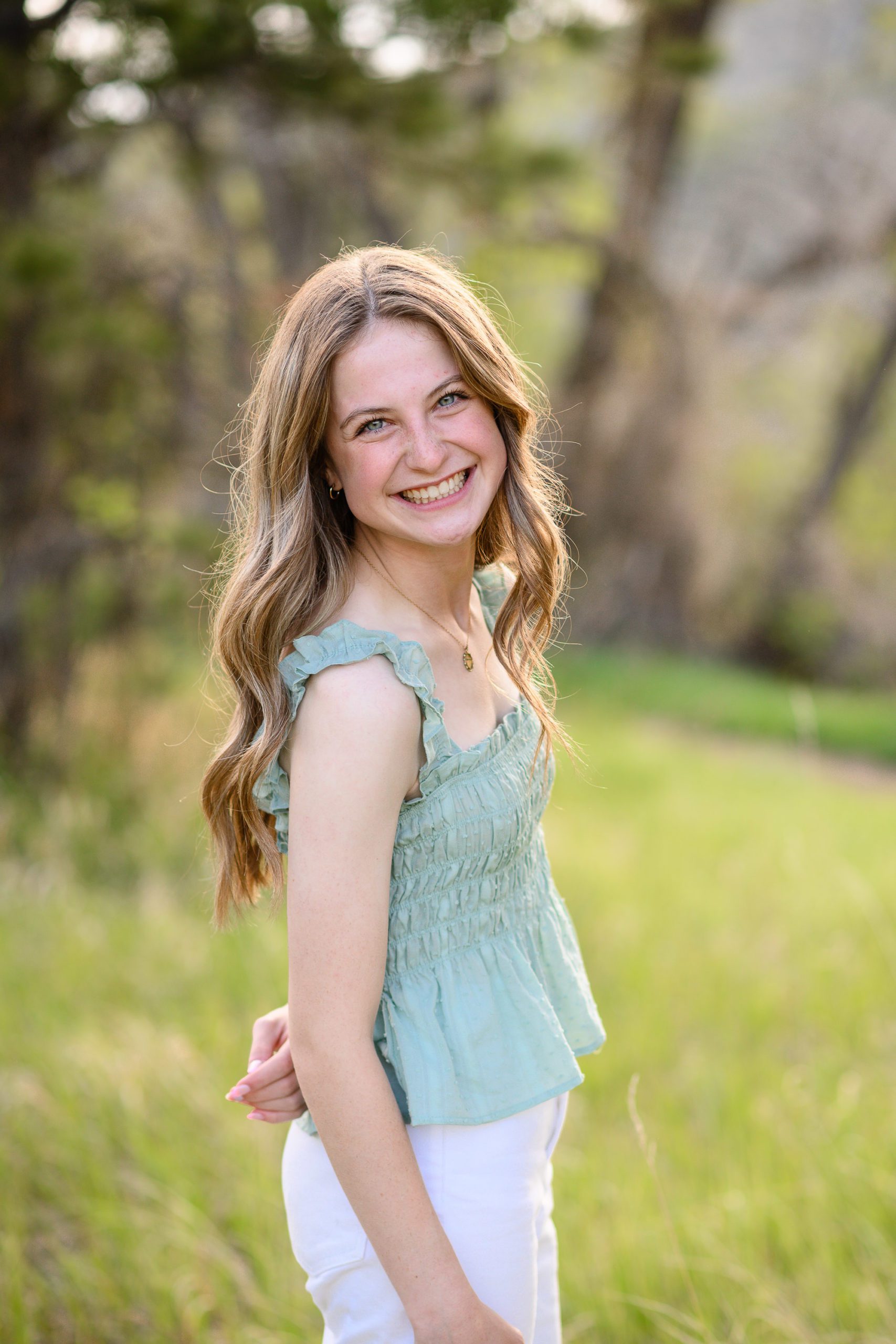 Senior girl in sunkissed light wearing a green frilled tank top looking over her shoulder at a Denver Senior Photographer.