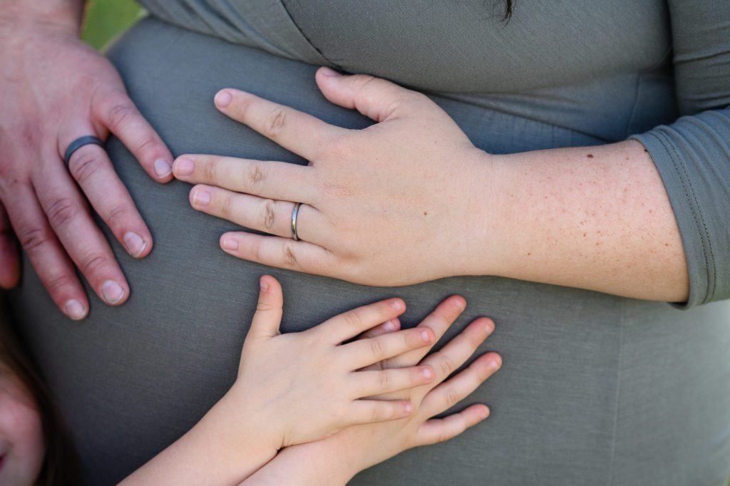 A closeup of a pregnant women with a green dress on with hands of the entire family touching her belly as captured by a Denver Photographer.