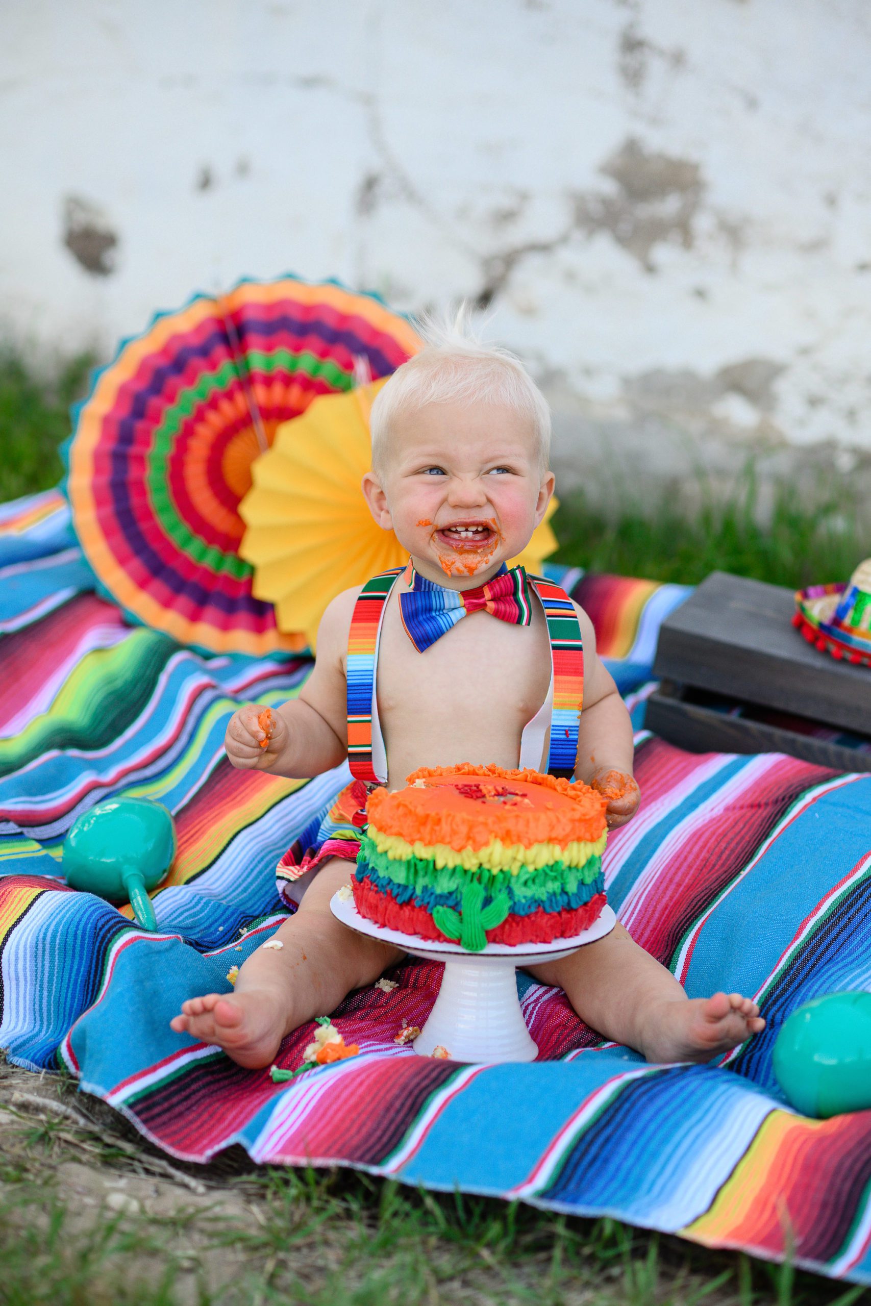 Denver Photographer captures a one year old boy sitting on a brightly colored Mexican blanket with fiesta props all around while he eats a brightly colored cake.