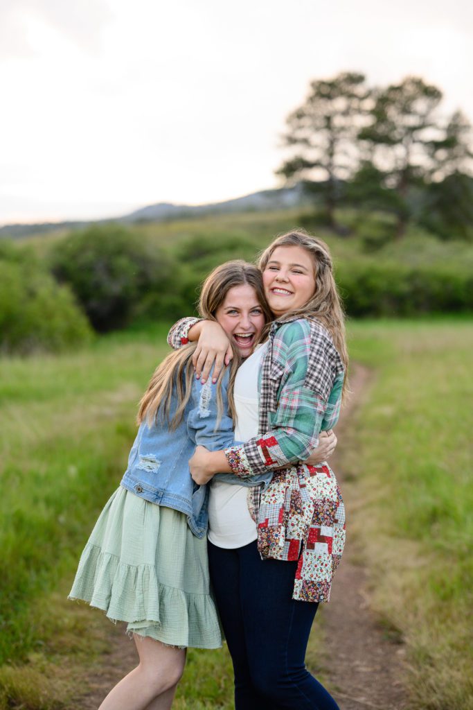 Two teen age girls hugging each other tightly as they stand in a mountain field as captured by a Denver Senior Photographer.
