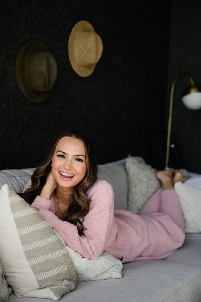 A woman in a pink fuzzy outfit lays on the couch facing the camera in a black office smiling at Denver Commercial Photographers.