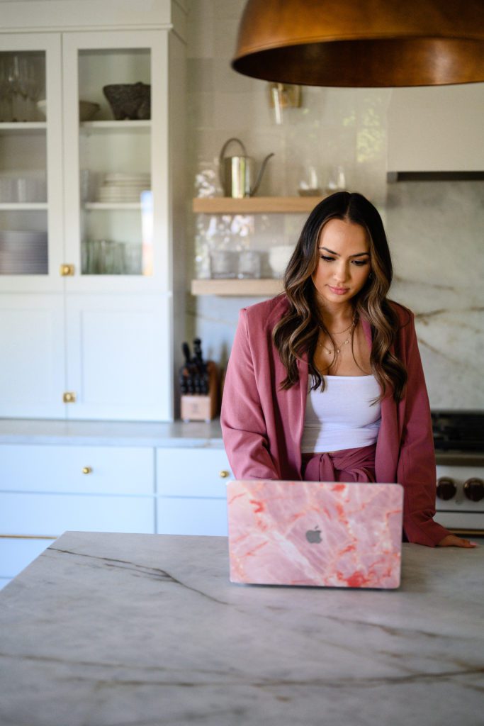 Woman standing in fancy kitchen looking at her pink laptop for her branding photos captured by denver commercial photographers