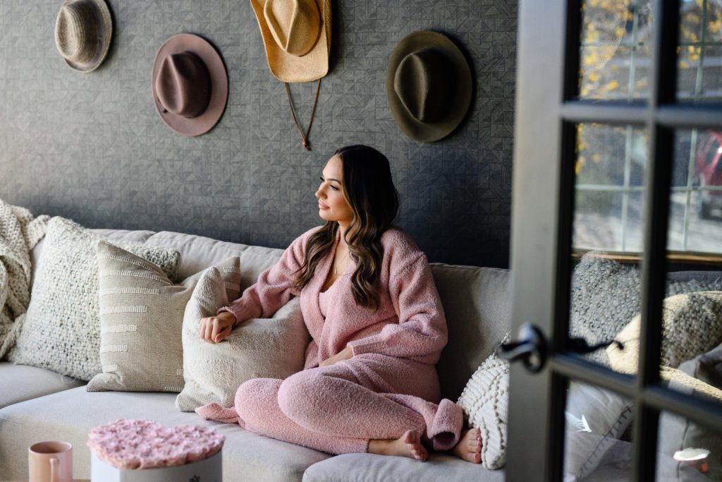 denver commercial photographers take lifestyle branding photos of a woman in a pink cozy outfit sitting on a couch looking out the window.