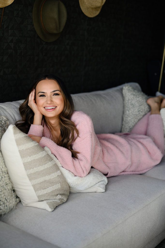 Woman in pink cozy outfit smiling at denver commercial photographers for her branding photos on a couch