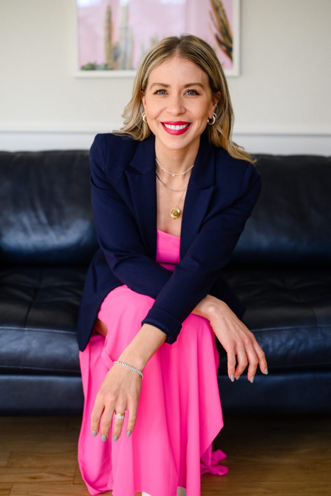 A woman on a blue couch in a bright pink dress smiling for her Denver Branding photos.