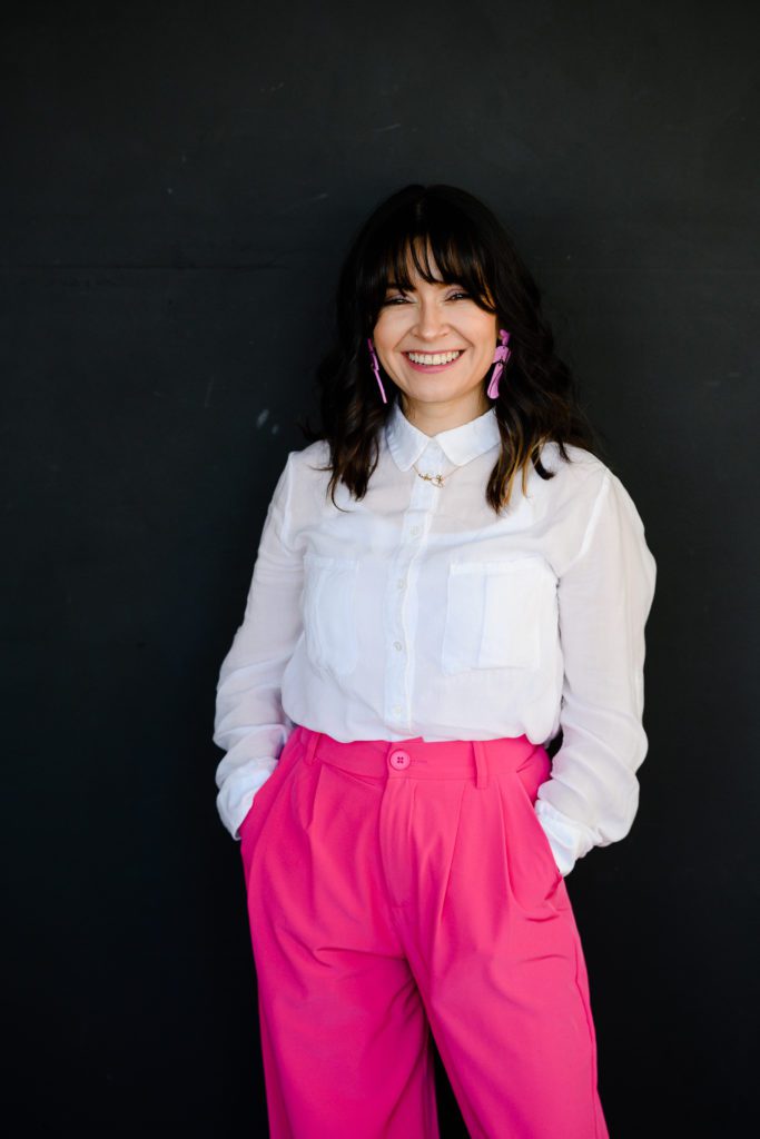 Dark haired woman with pink pants smiles at Denver commercial photographers during her branding photo session.