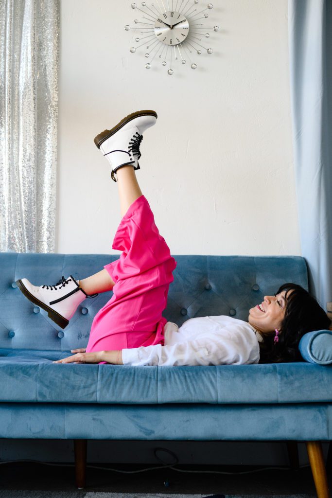 Denver Commercial Photographers captures personal branding photos of woman in pink pants and white combat boots laying on a blue velvet couch.