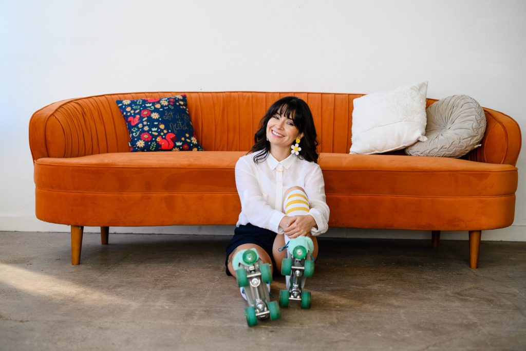 Denver Commercial Photographers capture dark haired woman wearing roller skates leaning against gorgeous orange couch.