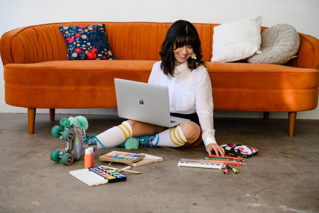 Denver Commercial Photographers captures personal branding photos of creative woman leaning against orange couch, wearing roller skates while doing art.