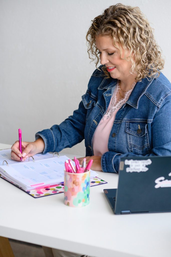 Denver Commercial Photographers captures woman with blonde curly hair looking down at her planner writing, wearing a jean jacket.