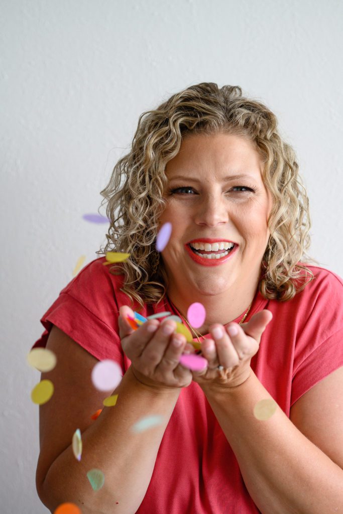 Denver Commercial Photographers captures woman wearing pink top holding confetti with blonde hair for personal branding photos.