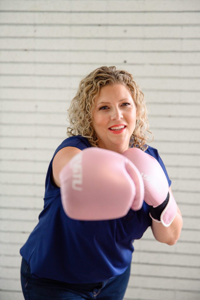 Fierce curly haired woman wears boxing gloves smiles for Denver Commercial Photographers