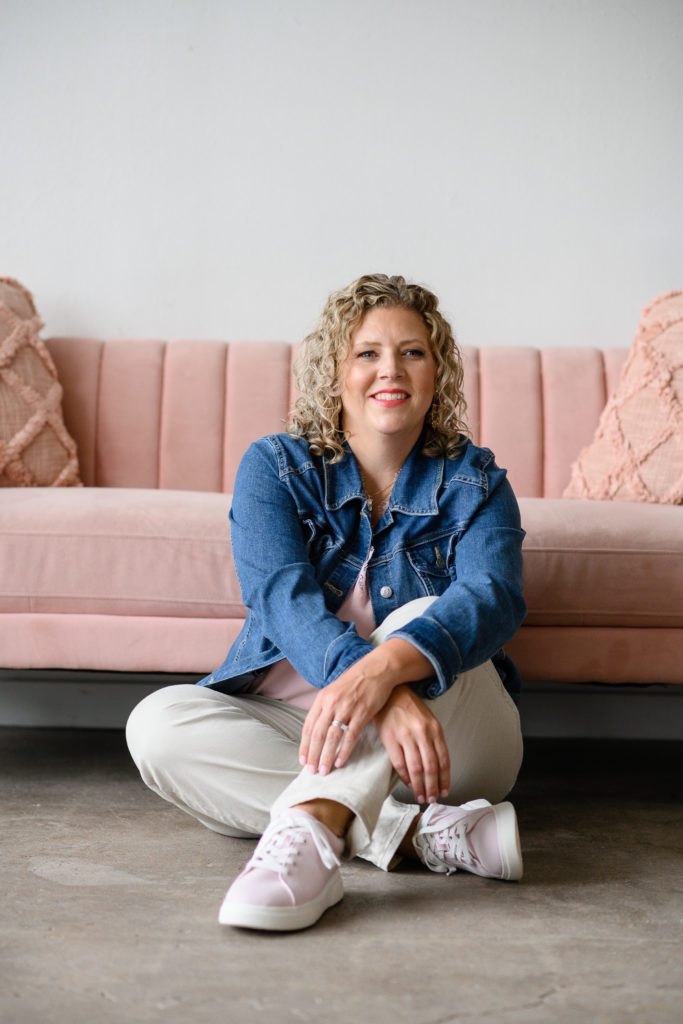 Denver Commercial Photographers captures personal branding photos of woman wearing a jean jacket leaning against a pink couch.