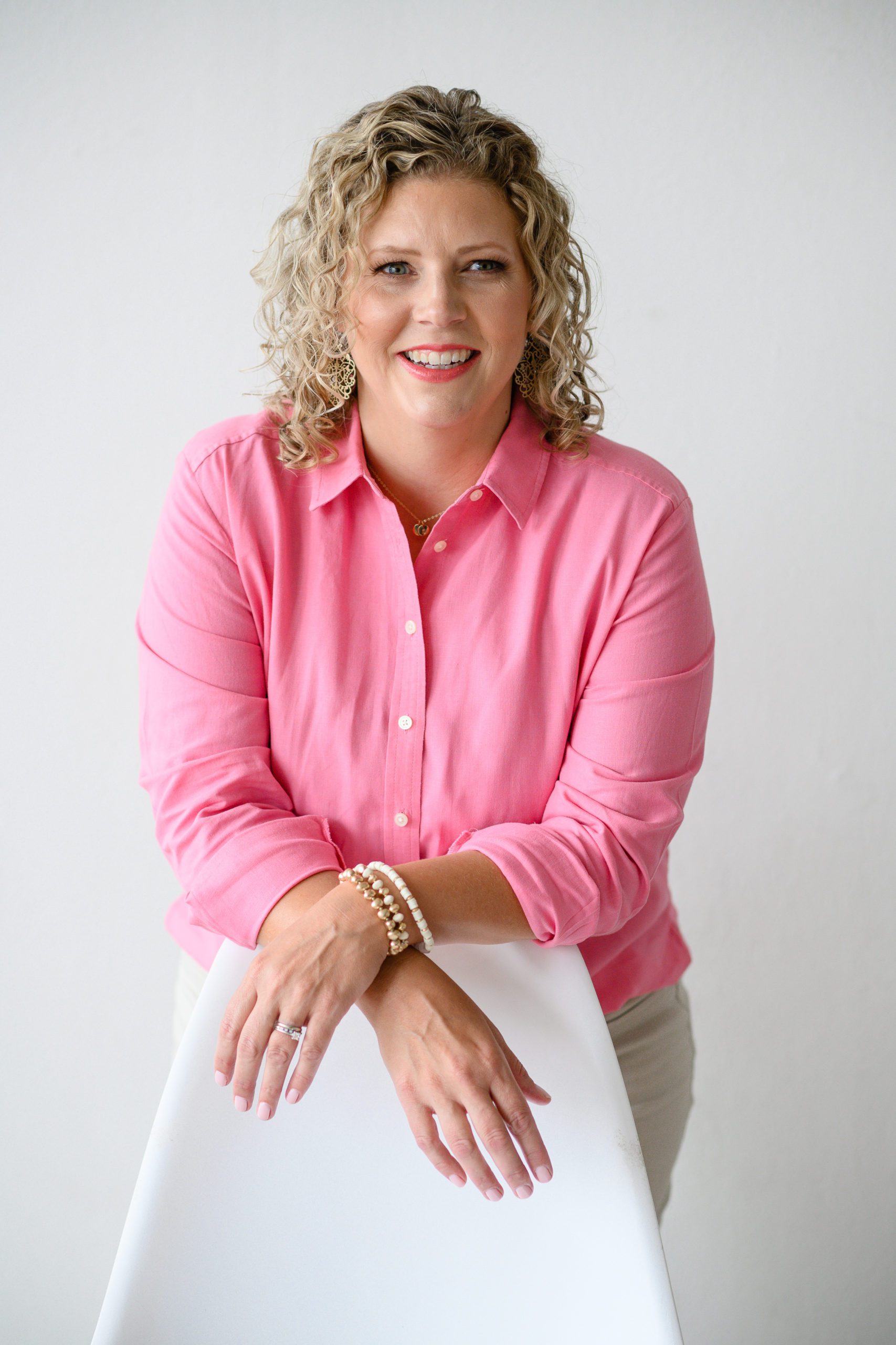 Denver Commercial Photographers captures woman wearing bright pink top leaning against a white chair.
