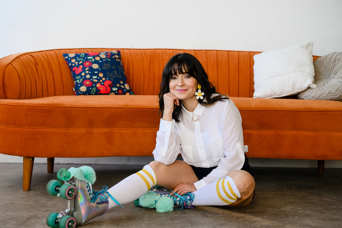 unique backdrops for branding photos with woman sitting in front of a bright orange couch in a studio space while wearing roller skates and tall socks
