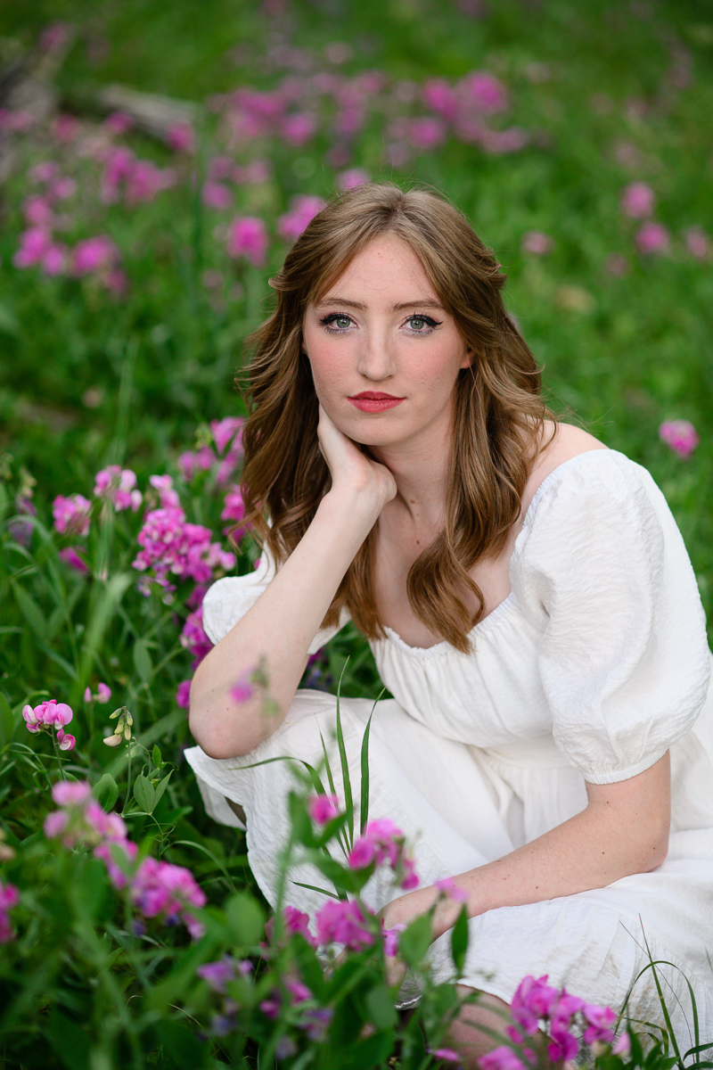 denver senior photographer photographs denver senior photos with woman in a white dress sitting in a field of purple wildflowers