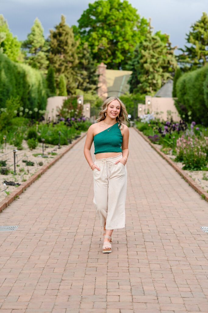 senior pictures with denver senior photographer capturing young woman walking down a brick path with her hands in her pockets in denver botanical gardens