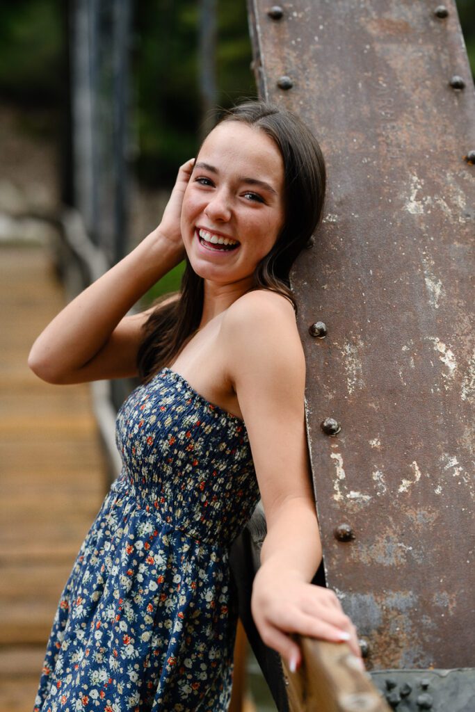 A girl smiles at a Denver senior photographer as she leans on a bridge in Aspen Colorado