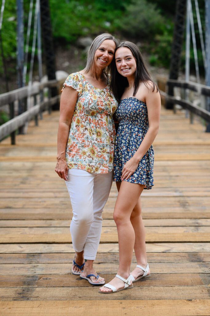 Mom and daughter smile at a Colorado senior photographer while standing on a bridge in Aspen colorado