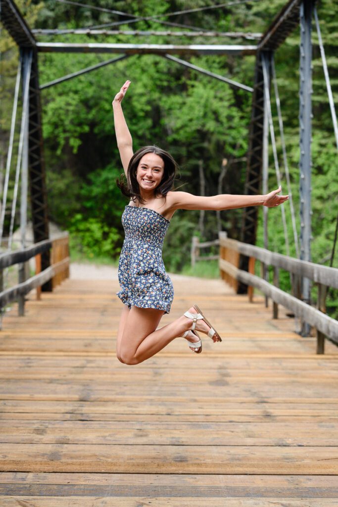 A senior girl jumps up on a bridge in Aspen Colorado for her Colorado senior photographer