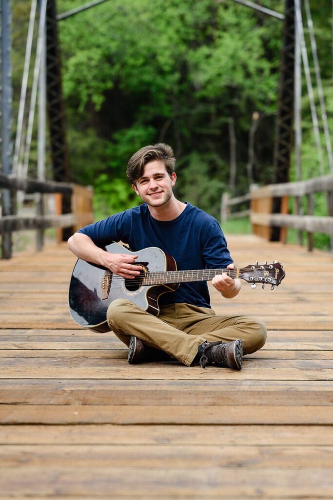 A senior boy with a guitar sits on a bridge in Aspen colorado for his Colorado Mountain senior pictures