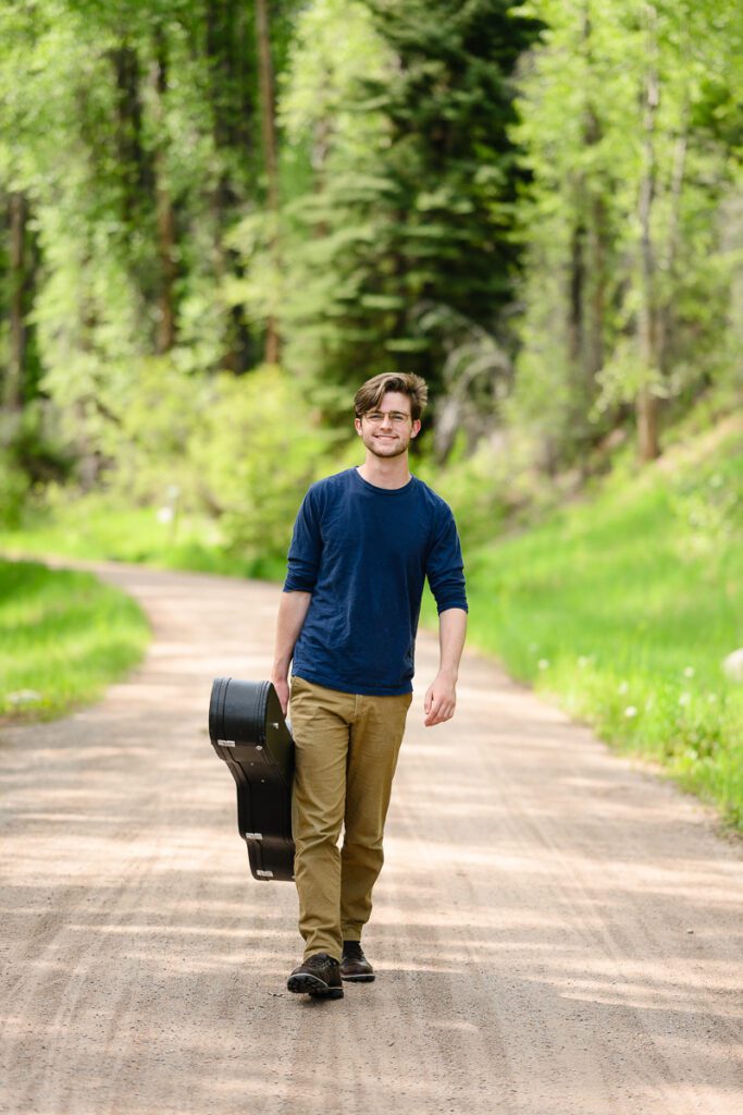 A guy carrying a guitar case walks toward the camera of a Colorado senior photographer