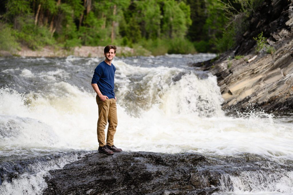 A senior boy stands in front of a waterfall in Aspen for his Colorado mountain senior pictures