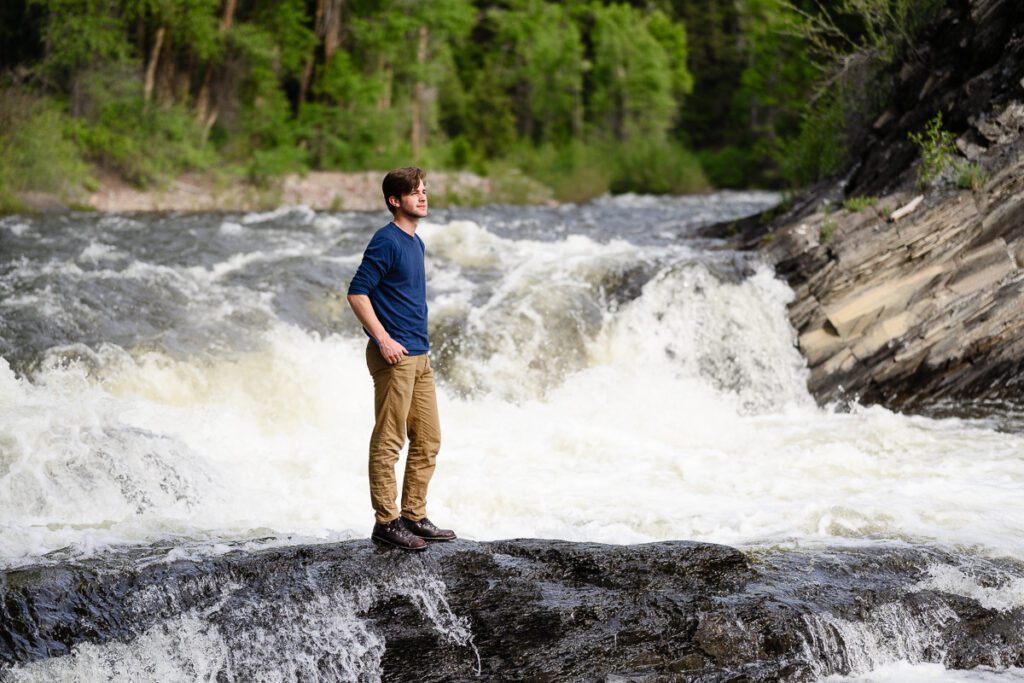 A senior guy stands in the middle of a waterfall in Aspen for his senior photos taken by a Denver senior photographer